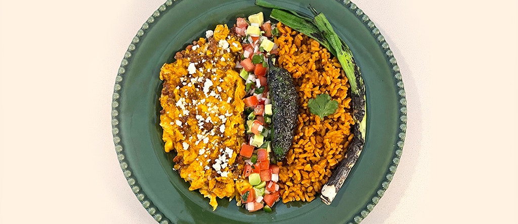 green plate with huevos con chorizo on spanish rice topped with a spicy avocado pico